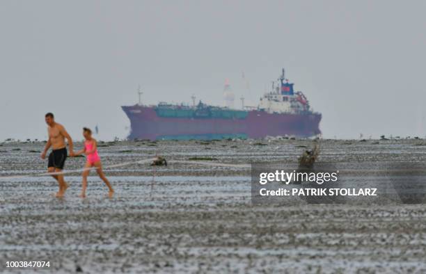 People walk in the mud in front of a ship on the sidelines of the "Duhner Wattrennen" mud flat race in Cuxhaven, northern Germany on July 22, 2018. /