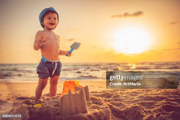 glückliche kleine junge gebäude sandburg am strand im sonnenuntergang - kind sandburg stock-fotos und bilder