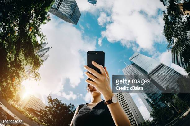 young businesswoman using mobile phone in city urban park against financial skyscrapers on a fresh bright morning - executive search bildbanksfoton och bilder