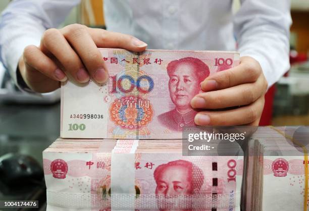 An employee counts 100-yuan notes at a bank in Nantong in China's eastern Jiangsu province on July 23, 2018. - China on July 23 rejected accusations...