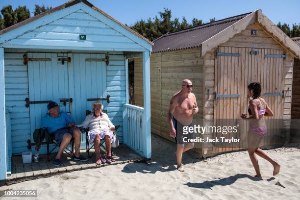 Couple shelter in the shade of a beach hut on West Wittering Beach during hot weather on the first day of the Summer school holidays on July 23, 2018...
