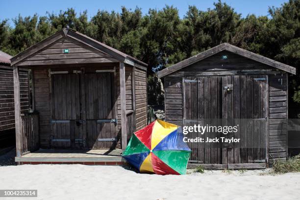 Parasol sits between two beach huts on West Wittering Beach during the hot weather on the first day of the Summer school holidays on July 23, 2018 in...
