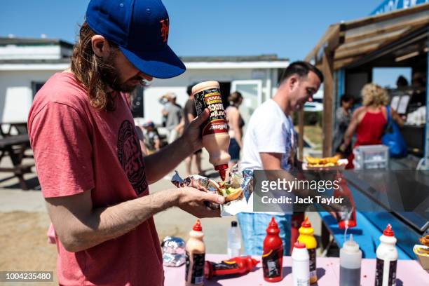 Beachgoers add sauce to their food at a stall by West Wittering Beach during hot weather on the first day of the Summer school holidays on July 23,...