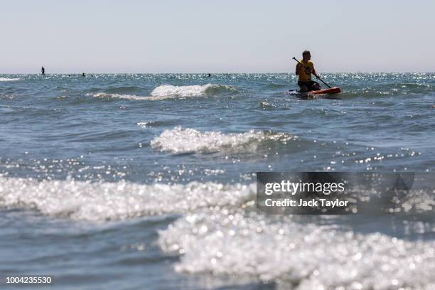 Paddle boarder sits on the water on West Wittering Beach during hot weather on the first day of the Summer school holidays on July 23, 2018 in...