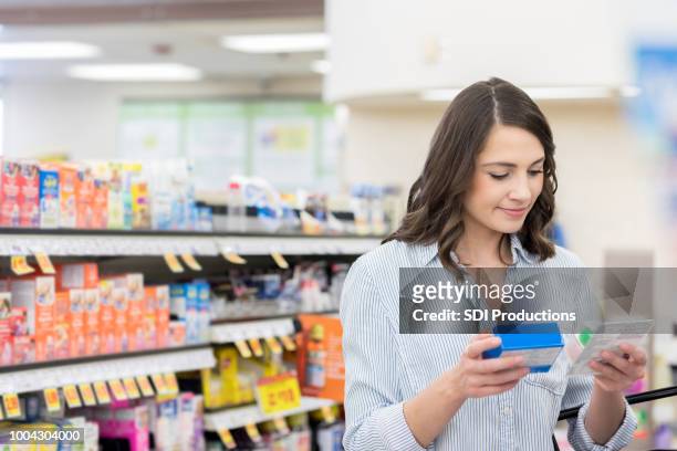 young woman compares medicine labels in pharmacy - comprare stock pictures, royalty-free photos & images