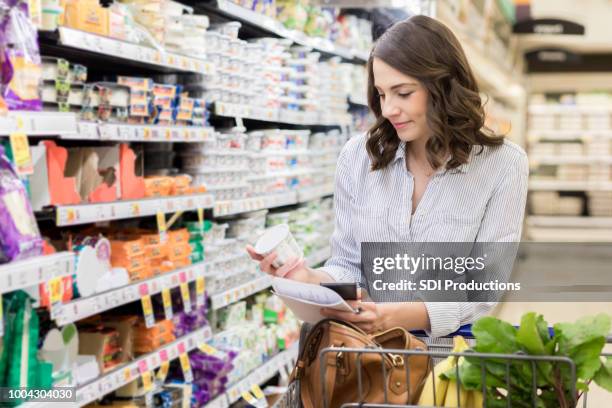 jovem mulher verifica ingredientes iogurte durante as compras de supermercado - passagem objeto manufaturado - fotografias e filmes do acervo