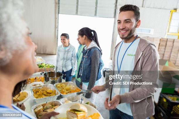 junger mann dient ältere frau bei food bank wohltätigkeitsaktion - soup kitchen stock-fotos und bilder