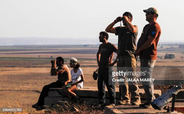 Picture taken on July 23, 2018 from the Israeli-annexed Golan Heights shows Israelis looking out across the border watching as warplanes backing a...