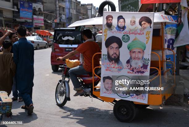 In this picture taken on July 2 Pakistani men walk past an election poster of a candidate from the Sunni Muslim religious party Tehreek-e-Labbaik...
