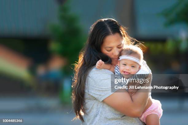 one year old baby with down syndrome is kissed by mother in the sun - down syndrome care stockfoto's en -beelden