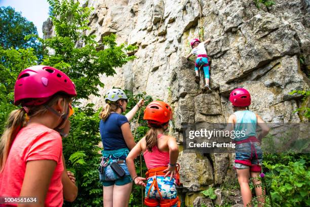 girls learning to climb from a female rock climbing instructor outside on a cliff face - escalar rochas imagens e fotografias de stock