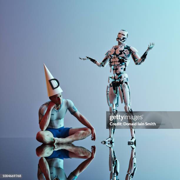 man sits wearing dunce hat beside white robot standing with arms raised - android stockfoto's en -beelden