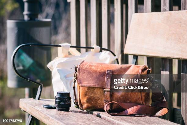 close-up image of a leather camera bag on a park bench in a sunny day (outdoors) - camera bag stock-fotos und bilder