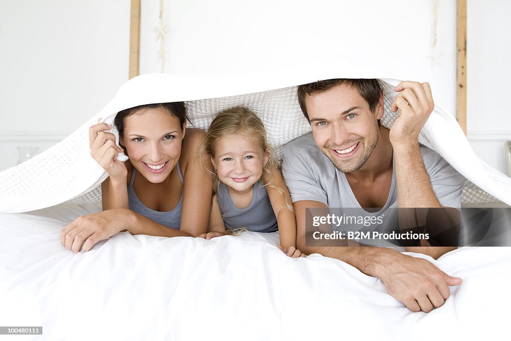 Parents with daughter lying under bed cover