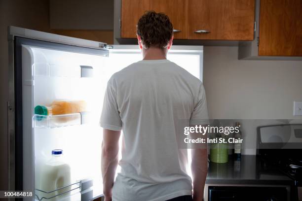 man standing looking at contents of fridge - appetite stock pictures, royalty-free photos & images