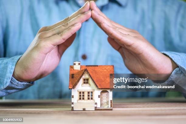 hands covering a toy house. home protection concept - seguro del hogar fotografías e imágenes de stock