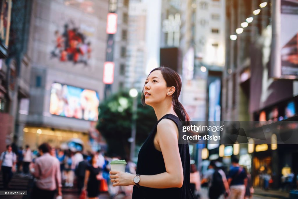 Beautiful young Asian woman holding coffee visiting and exploring in the busy downtown city street of Hong Kong