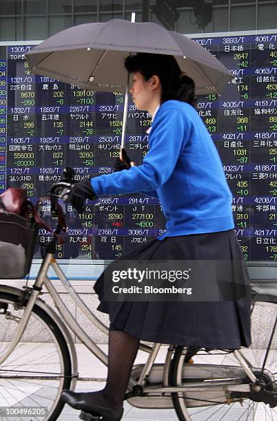 Woman cycles past an electronic stock board outside a securities firm in Tokyo, Japan, on Tuesday, May 25, 2010. Japanese stocks fell, dragging the...