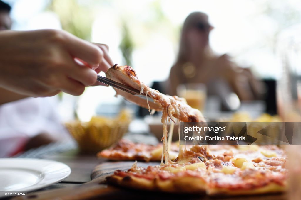 Hand pulling up cheesy slice of pizza at an outdoor restaurant table