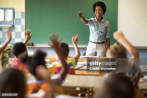 happy african american elementary teacher aiming at school kid to answer her question. - teachers imagens e fotografias de stock