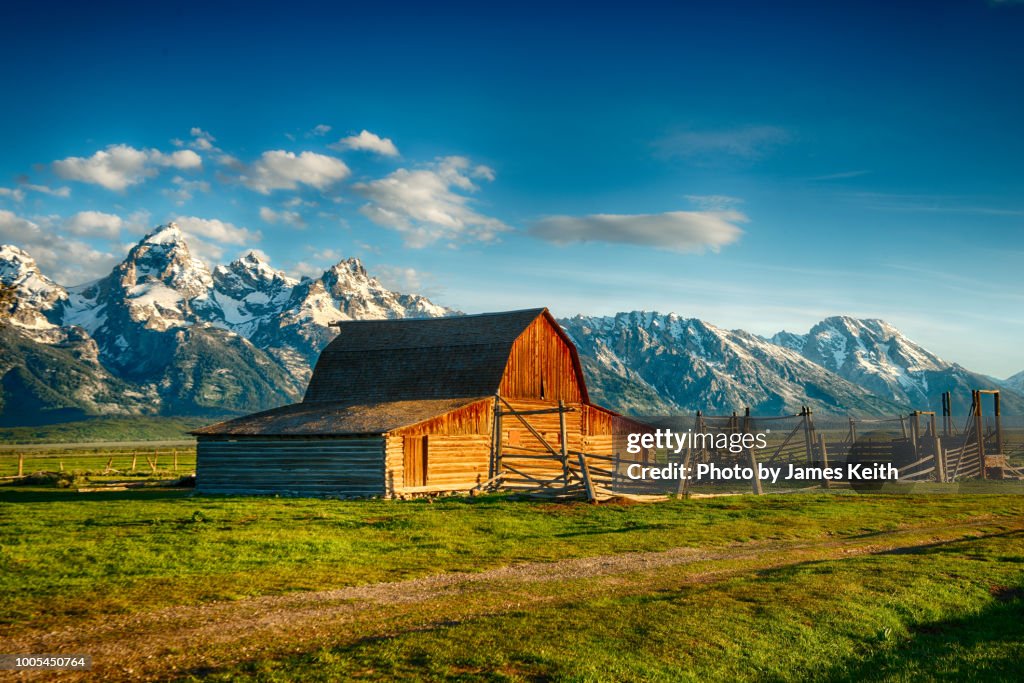 A rising sun illuminates the John Moulton homestead's barn and corrals with the magnificent Tetons as a backdrop.