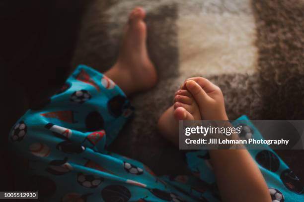 toddler holds foot and toes after hand, foot, and mouth disease - sick kid fotografías e imágenes de stock