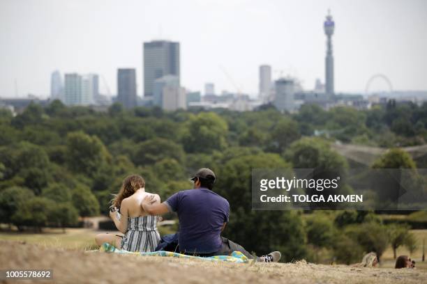 Visitors to Primrose Hill apply sunscreen cream as they sit on the dry brown grass in London on July 26, 2018. - Britain has been in the grip of its...