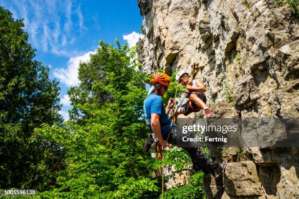 a rock climbing instructor assists a child on a rock face - abseiling stock pictures, royalty-free photos & images