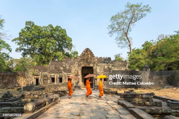 three monks with umbrellas walking inside a temple - siem reap stockfoto's en -beelden