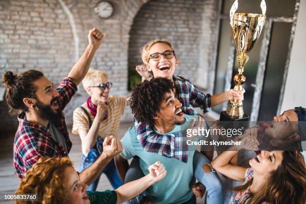 large group of happy creative people celebrating getting a trophy at casual office. - trophy award stock pictures, royalty-free photos & images