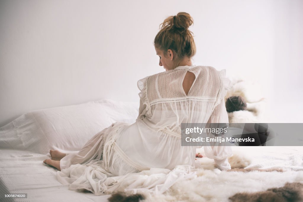 Beautiful woman lying in bed in white dress