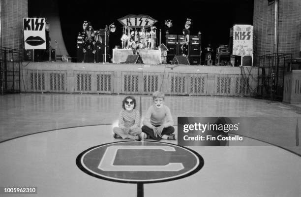 American rock group Kiss conduct a sound check on the stage of Cadillac High School gymnasium as two young face-painted fans sit cross legged on the...