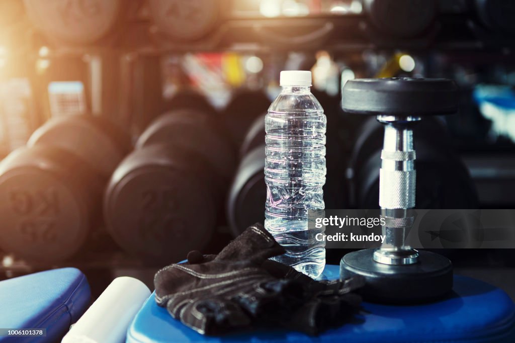 Fitness and workout concept, fresh water bottle in gym with dumbbell.