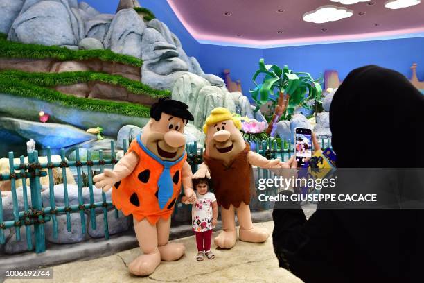 Employees wearing a Fred Flintstone and Barney Rubble costume pose for a picture with a girl at Warner Bros. World, the first-ever Warner branded...