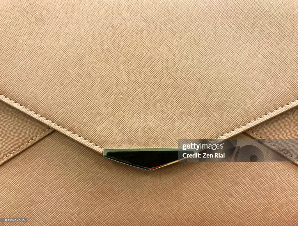 Front view of a light brown purse showing edge of flap and metal decor