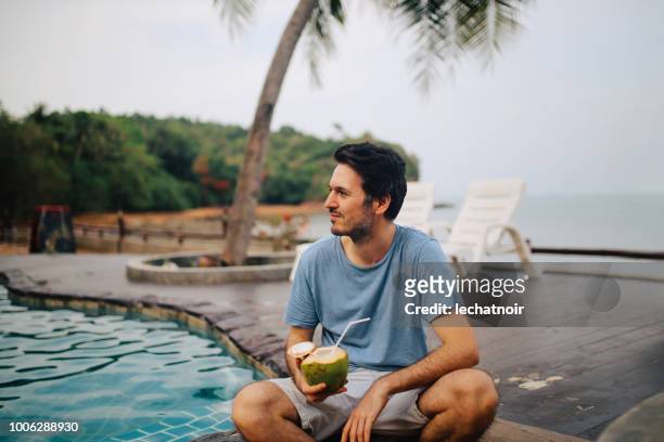 young man having a fresh coconut drink by the ocean on the island of koh lanta, thailand - coconut water stock pictures, royalty-free photos & images