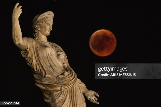 Picture shows the full moon during a "blood moon" eclipse beside a statue of ancient Greek goddess Hera in central Athens on July 27, 2018. - The...