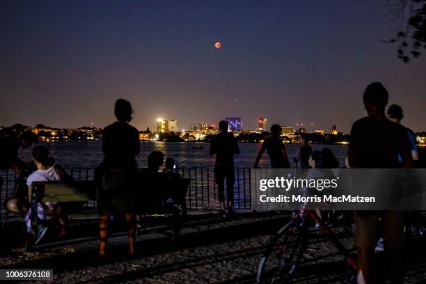 People gather at the Alster Lake to watch the 'blood moon' eclipse over the northern German city of Hamburg on July 27, 2018. During this eclipse,...