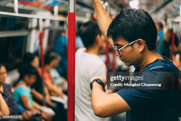 young man traveler is visiting at hongkong by subway mtr train and looking watch. the mass transit railway is the rapid transit railway system in hong kong. - crowded bus stock pictures, royalty-free photos & images