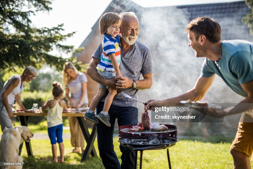 Glückliche Großvater und Enkel sprechen für junge Vater Vorbereitung Grill im Garten.