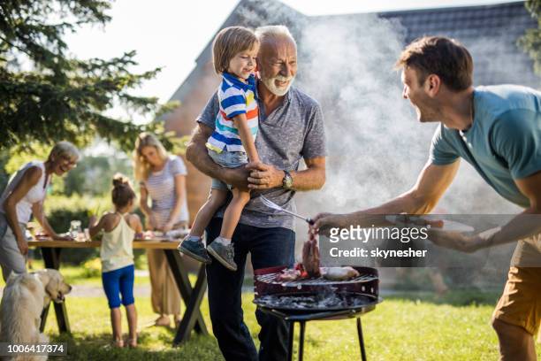 feliz avô e neto falando aos jovens pai preparando churrasco no quintal. - grelha de churrasco - fotografias e filmes do acervo