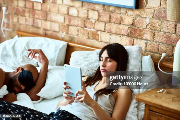 young woman reading e book in bed as man sleeps - computer wearing eye mask stock pictures, royalty-free photos & images