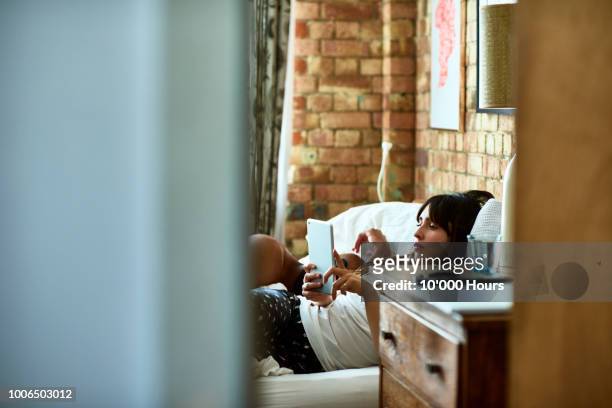 view through doorway towards woman reading in bed - bedroom doorway stock pictures, royalty-free photos & images