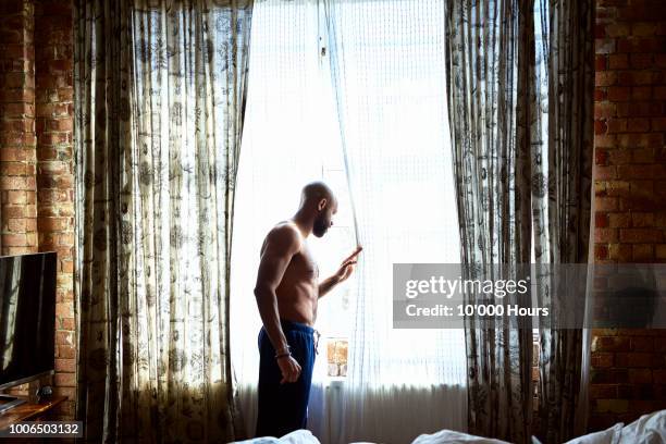 mid adult man looking out of window in hotel room - awake day stockfoto's en -beelden