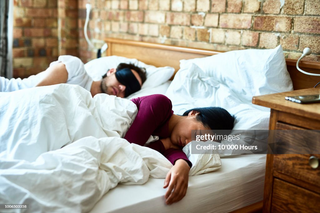 Woman asleep with hand on mattress and man wearing eye mask