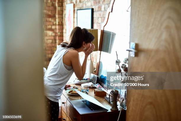 young woman in vest top applying make up in mirror - 鏡台 ストックフォトと画像