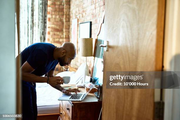 man with coffee checking emails on laptop in bedroom - ahora fotografías e imágenes de stock