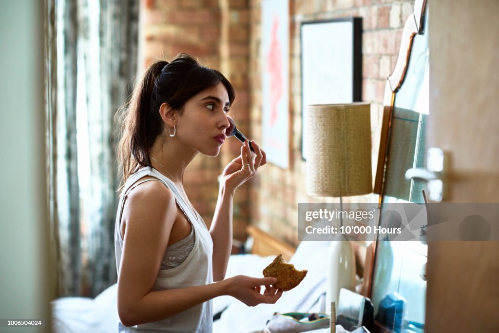 Young woman applying blusher with make up and holding toast
