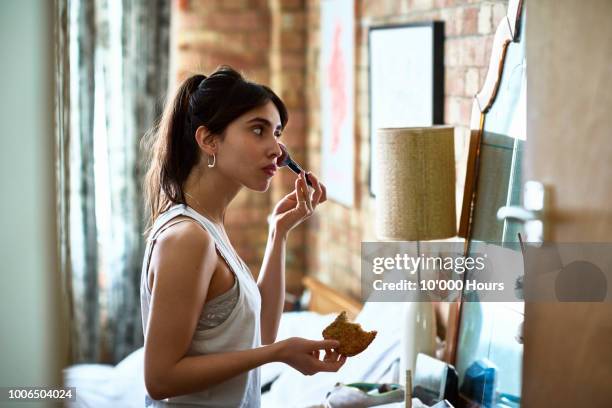 young woman applying blusher with make up and holding toast - applying makeup stockfoto's en -beelden