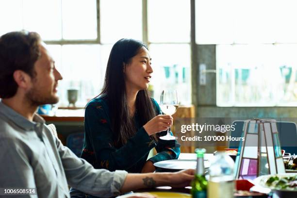 attractive chinese woman with white wine listening at dinner party - suave stock pictures, royalty-free photos & images